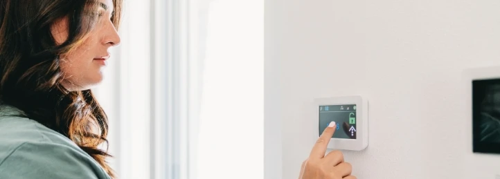 Woman adjusting a smart thermostat on a wall to control home temperature.